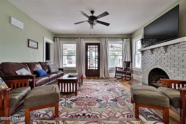 living area featuring a brick fireplace, baseboards, a ceiling fan, and wood finished floors