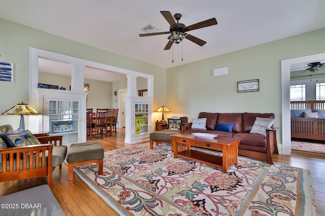 living area featuring wood finished floors, visible vents, ornate columns, and ceiling fan