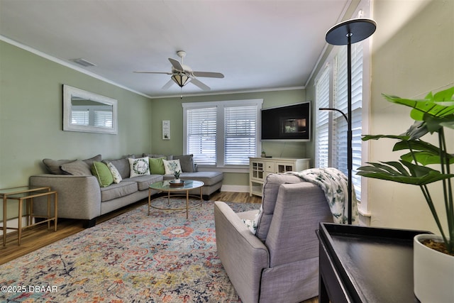 living area featuring visible vents, wood finished floors, crown molding, baseboards, and ceiling fan