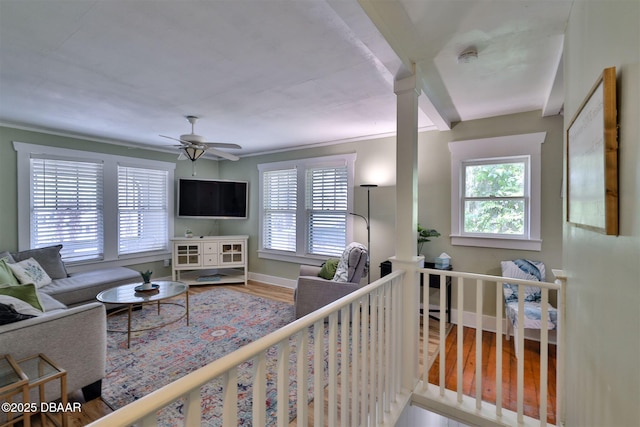 living area featuring baseboards, a healthy amount of sunlight, wood finished floors, and a ceiling fan