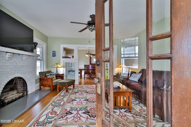 living area with wood finished floors, a brick fireplace, and a ceiling fan