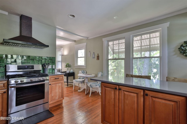 kitchen with light wood finished floors, crown molding, wall chimney range hood, brown cabinets, and stainless steel gas range