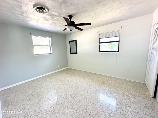 spare room featuring a wealth of natural light, baseboards, speckled floor, and ceiling fan