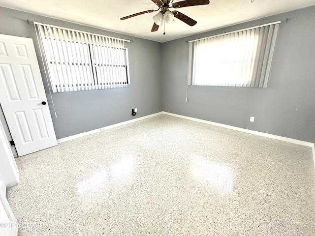 unfurnished room with speckled floor, baseboards, and a ceiling fan