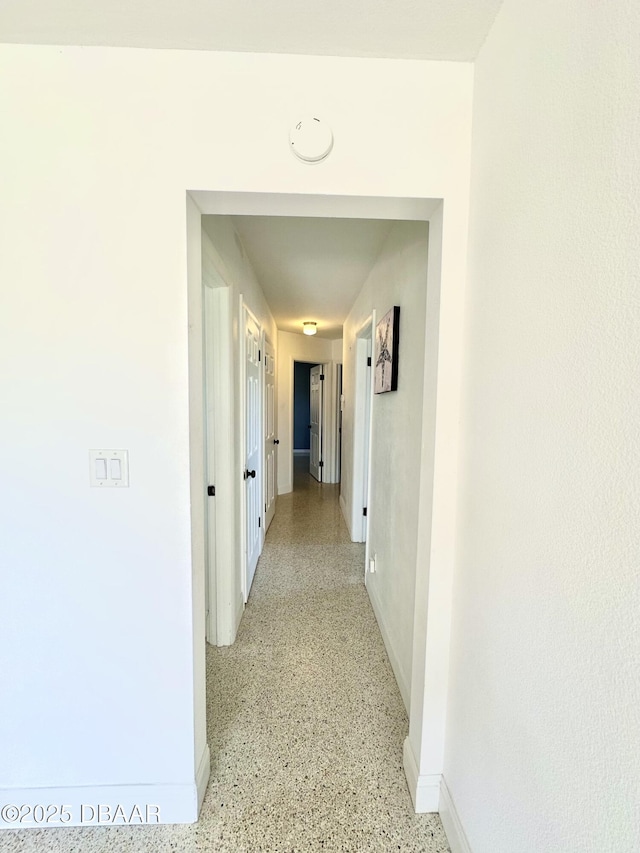 hallway with baseboards and light speckled floor