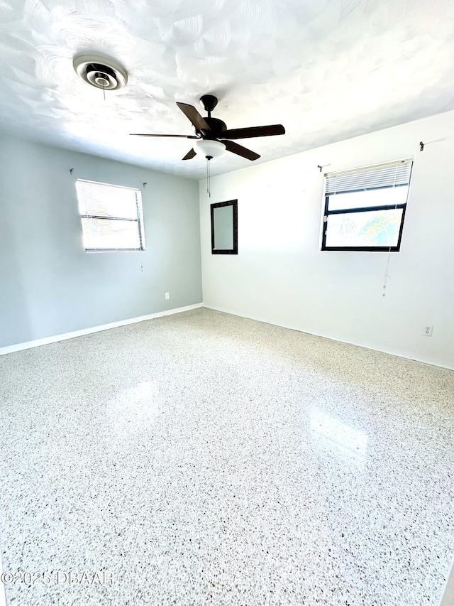 spare room with speckled floor, baseboards, a ceiling fan, and visible vents