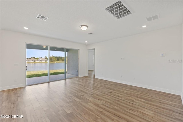 unfurnished room featuring light hardwood / wood-style floors, a textured ceiling, and a water view