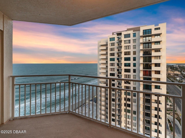 balcony at dusk featuring a water view