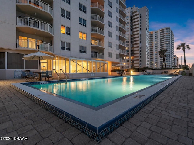 pool at dusk with a community pool and a patio