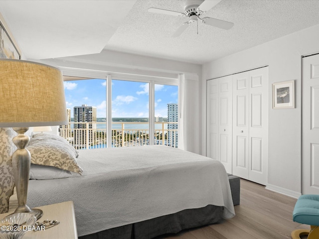 bedroom featuring baseboards, a water view, wood finished floors, and multiple windows