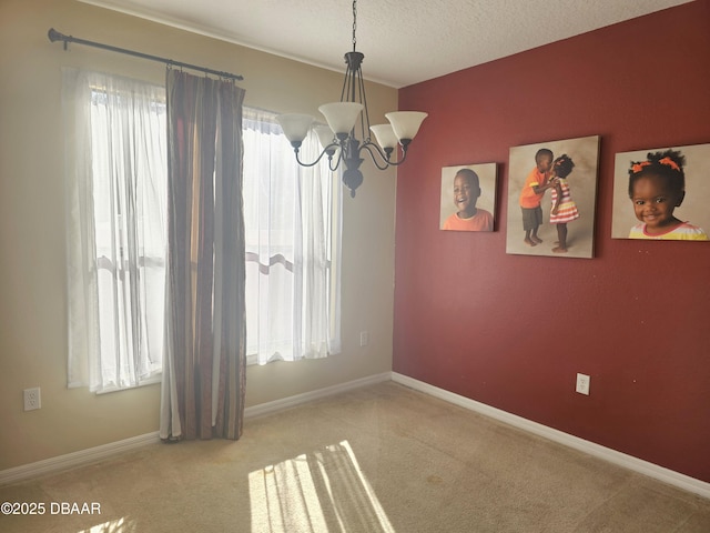 carpeted empty room with a textured ceiling, baseboards, and a chandelier