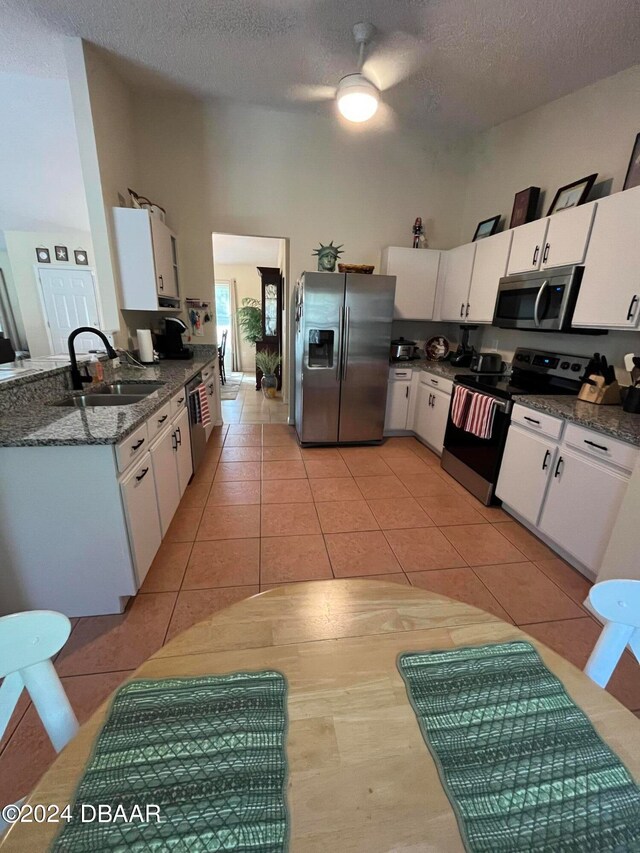 kitchen with stainless steel appliances, sink, light tile patterned floors, white cabinetry, and dark stone countertops