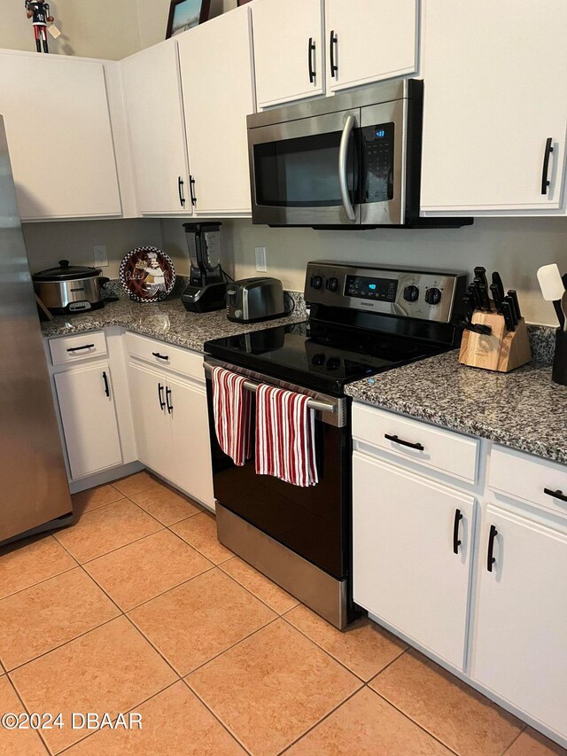 kitchen with white cabinets, appliances with stainless steel finishes, dark stone counters, and light tile patterned flooring