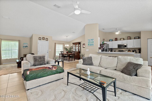 living room featuring a textured ceiling, ceiling fan with notable chandelier, lofted ceiling, and light tile patterned floors