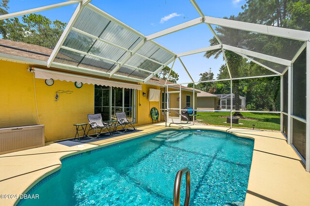 view of pool with glass enclosure, a lawn, and a patio