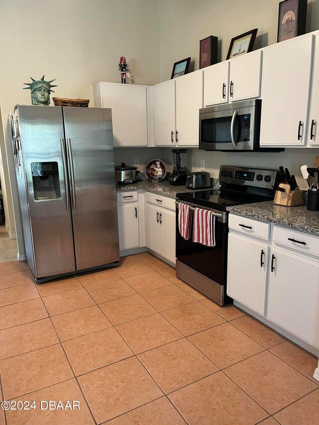 kitchen with stainless steel appliances, dark stone countertops, white cabinetry, and light tile patterned floors