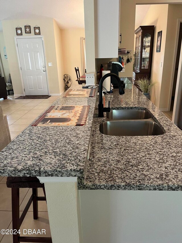 kitchen featuring light tile patterned flooring, stone countertops, sink, kitchen peninsula, and a kitchen bar