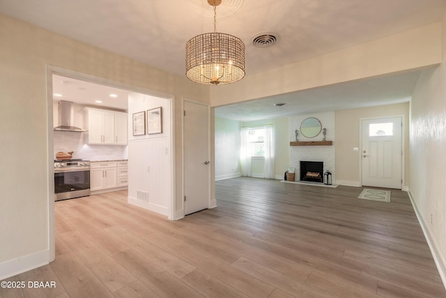 unfurnished living room with visible vents, an inviting chandelier, light wood-style floors, a brick fireplace, and baseboards