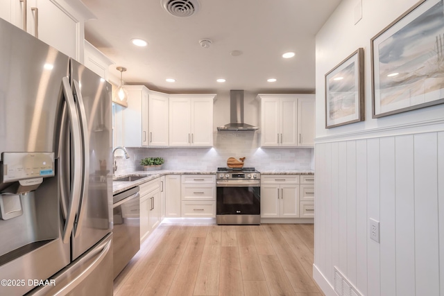 kitchen featuring visible vents, stainless steel appliances, wall chimney range hood, pendant lighting, and a sink