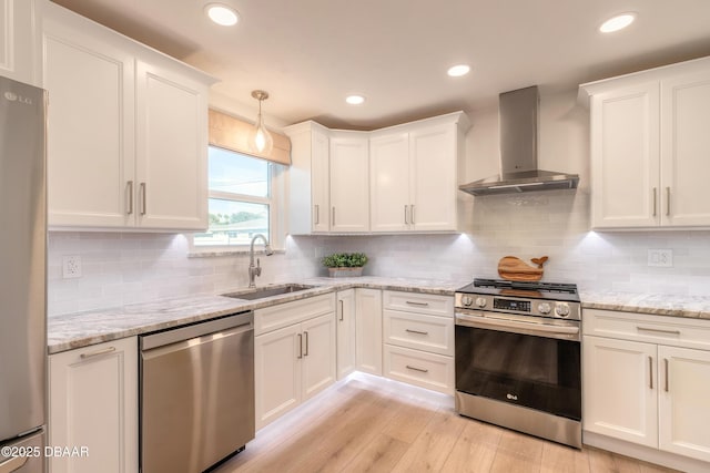 kitchen with pendant lighting, appliances with stainless steel finishes, white cabinetry, a sink, and wall chimney exhaust hood