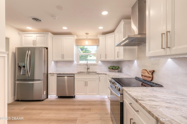 kitchen with a sink, white cabinets, appliances with stainless steel finishes, wall chimney range hood, and decorative light fixtures