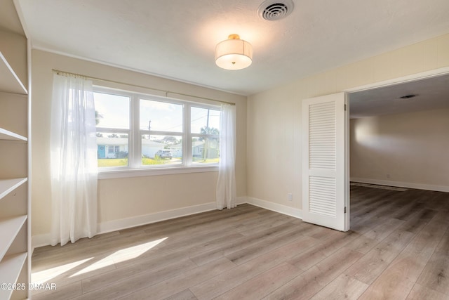 spare room with light wood-type flooring, visible vents, and baseboards