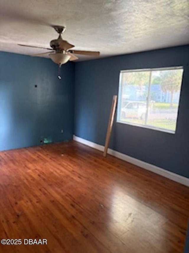 spare room featuring baseboards, wood finished floors, and ceiling fan