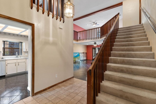 staircase with a high ceiling, a ceiling fan, tile patterned floors, and baseboards