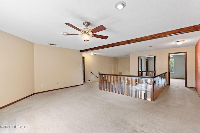 spare room featuring light colored carpet, beamed ceiling, and baseboards