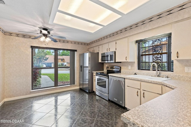 kitchen featuring light countertops, a sink, stainless steel appliances, ceiling fan, and dark tile patterned flooring