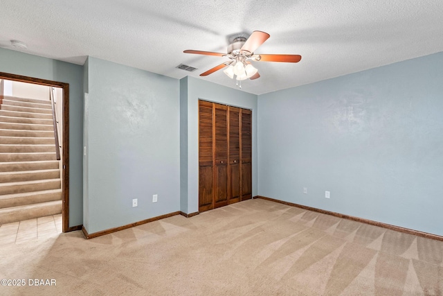 unfurnished bedroom with a closet, a textured ceiling, visible vents, baseboards, and light colored carpet