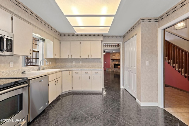 kitchen featuring light countertops, dark tile patterned flooring, a sink, white cabinets, and appliances with stainless steel finishes