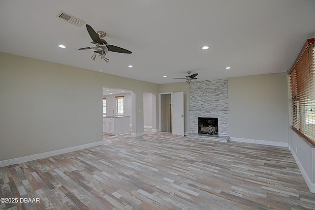 unfurnished living room with ceiling fan, a stone fireplace, sink, and light wood-type flooring