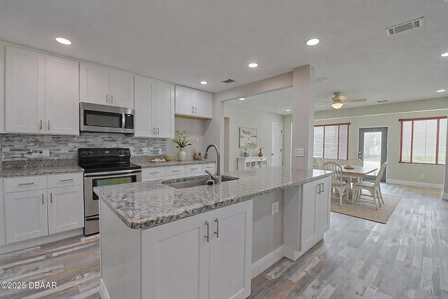 kitchen with stone counters, an island with sink, sink, white cabinets, and stainless steel appliances