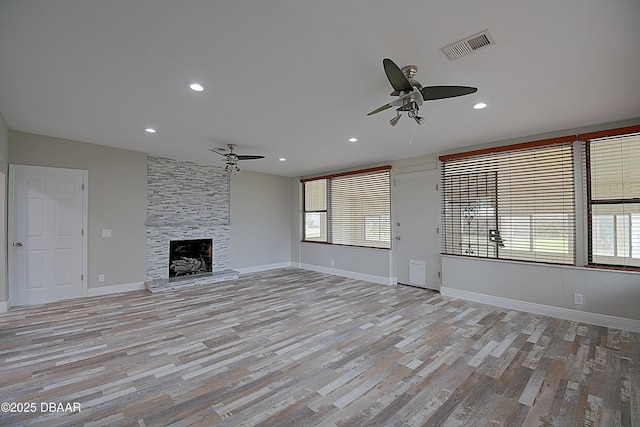 unfurnished living room featuring ceiling fan, a large fireplace, light wood-type flooring, and a wealth of natural light