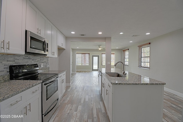 kitchen featuring light wood-style flooring, stainless steel appliances, a sink, a wealth of natural light, and backsplash