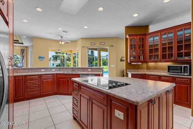 kitchen with a textured ceiling, stainless steel appliances, ceiling fan, light tile patterned floors, and a center island