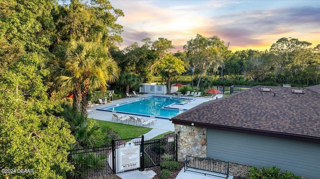 pool at dusk featuring a patio and a lawn