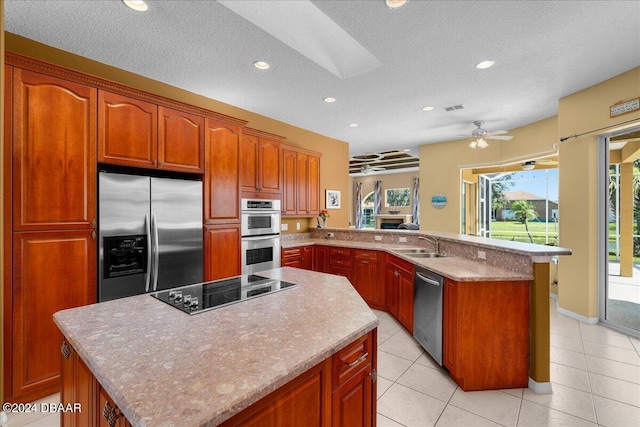 kitchen featuring kitchen peninsula, appliances with stainless steel finishes, a skylight, a textured ceiling, and ceiling fan