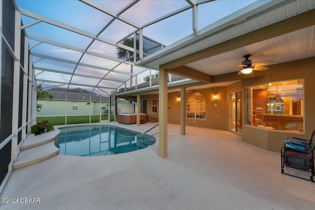 pool at dusk with a lanai, ceiling fan, a patio, and a hot tub