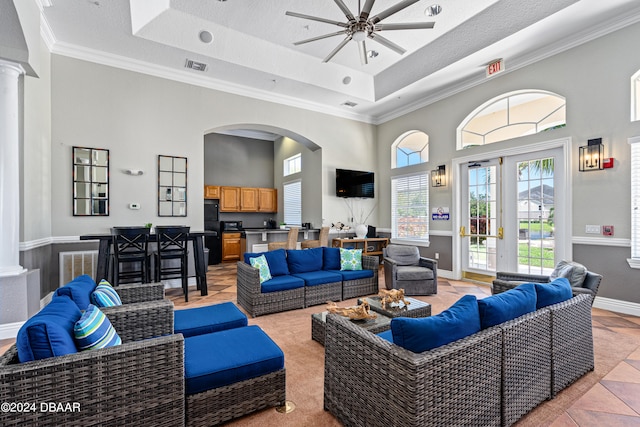 living room featuring a textured ceiling, decorative columns, ornamental molding, ceiling fan, and a high ceiling