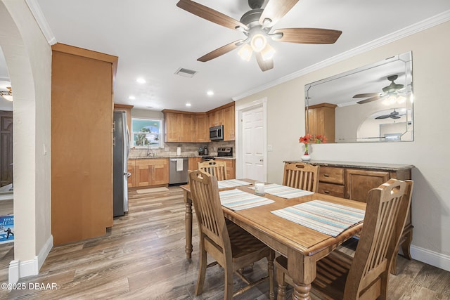 dining room with sink, crown molding, ceiling fan, and light wood-type flooring