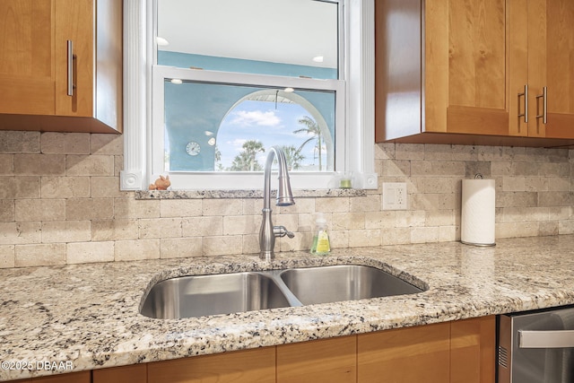 kitchen with light stone counters, stainless steel dishwasher, sink, and tasteful backsplash