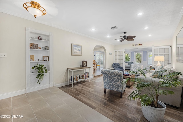 living room with crown molding, built in features, ceiling fan, and light wood-type flooring