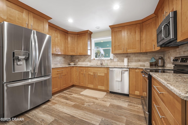 kitchen with sink, stainless steel appliances, light stone counters, decorative backsplash, and light wood-type flooring