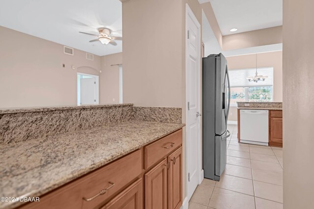 kitchen with light tile patterned flooring, white dishwasher, stainless steel refrigerator with ice dispenser, ceiling fan with notable chandelier, and light stone countertops