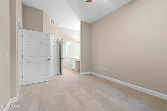 unfurnished bedroom with ceiling fan, connected bathroom, light carpet, and high vaulted ceiling