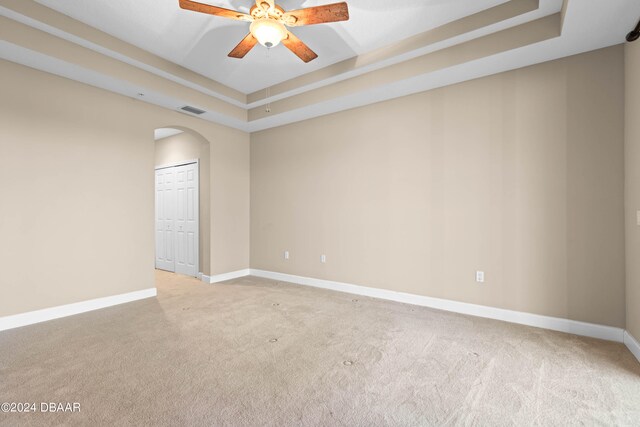 carpeted spare room with a tray ceiling and ceiling fan