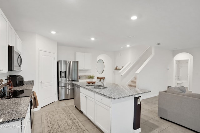 kitchen with white cabinetry, stainless steel appliances, a center island with sink, and light stone counters