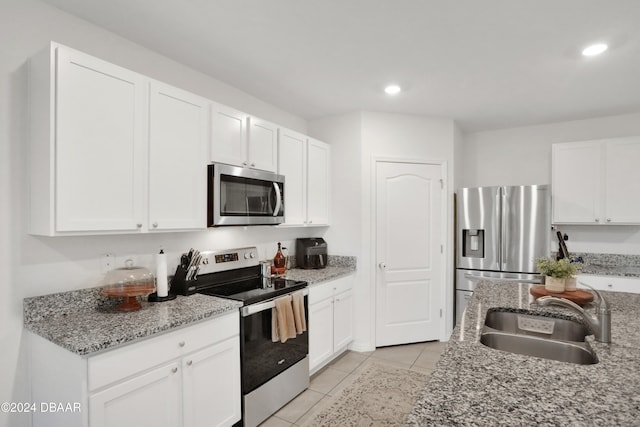 kitchen with light stone counters, white cabinetry, appliances with stainless steel finishes, light tile patterned floors, and sink